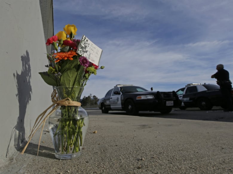 Flowers are left by the side of the road on December 3, 2015, as a San Bernardino police officer blocks the road leading to the site of a Dec. 2 mass shooting in San Bernardino, Calif. 